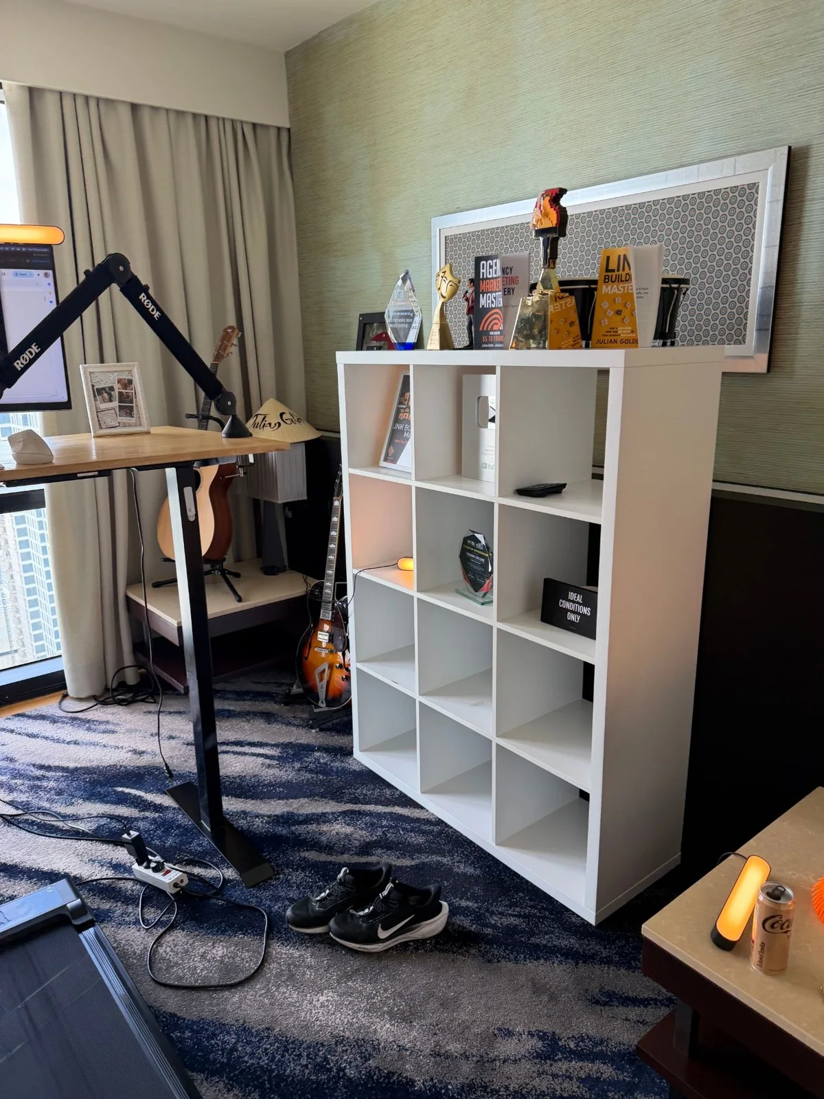 The other side of Julian's office: a white shelf with awards and books, guitars on stands, and the standing desk with the Rode boom arm